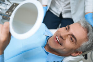 Man smiling in the mirror after bone graft and dental implant procedures
